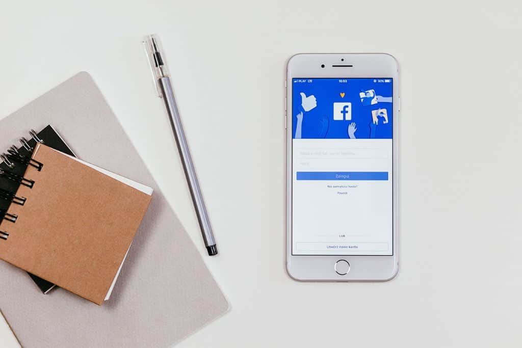Smartphone displaying Facebook app with advertising icons, on desk with notebooks and pen.