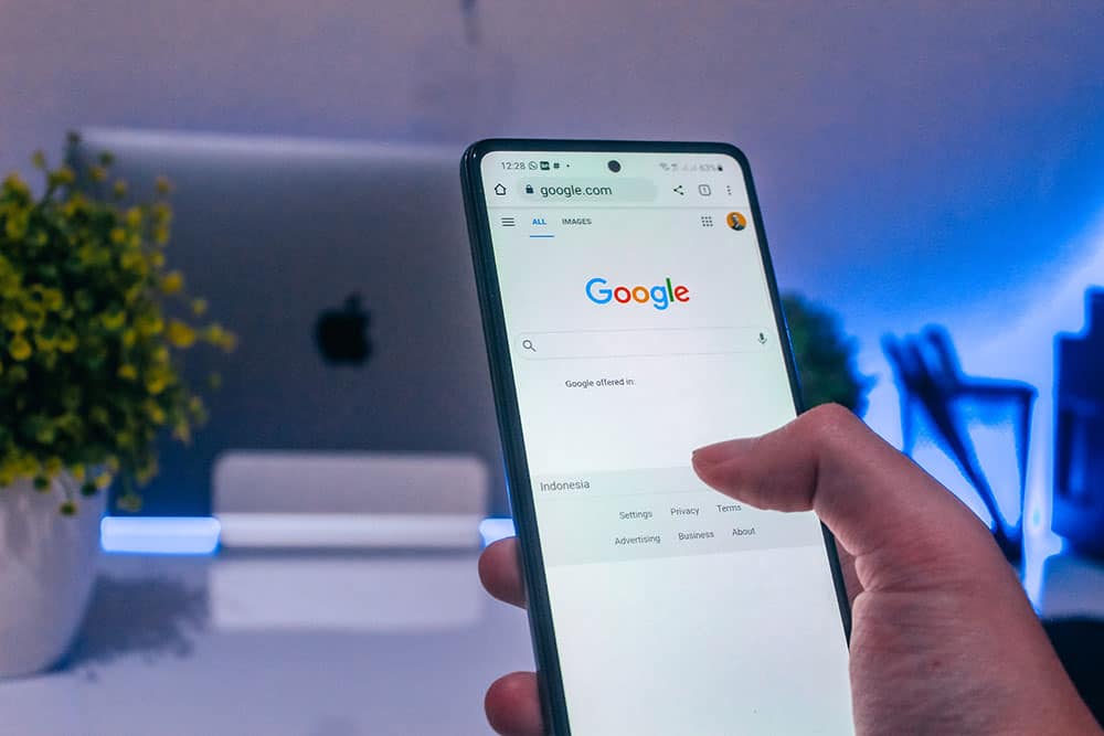 Person using a smartphone to access Google search on a desk.