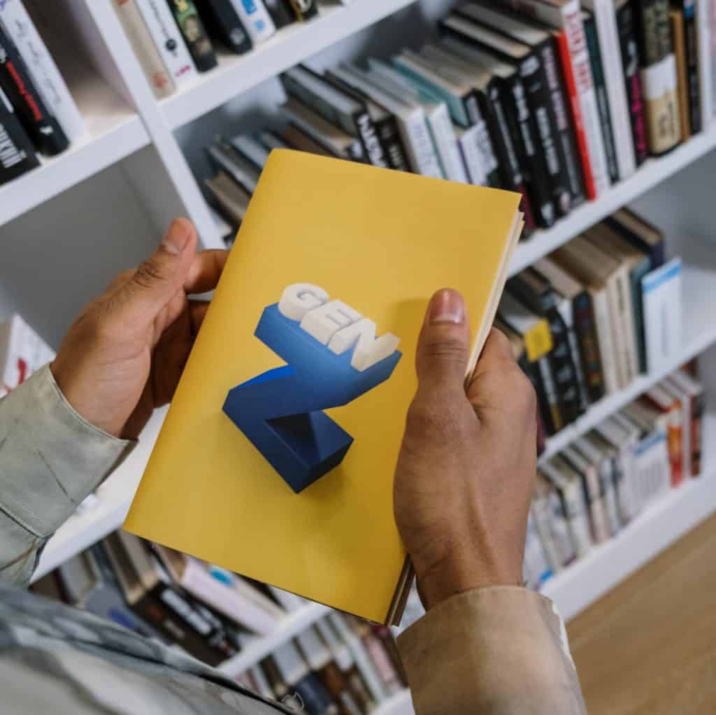 Person holding a yellow book with "GEM" 3D letters in a library setting.