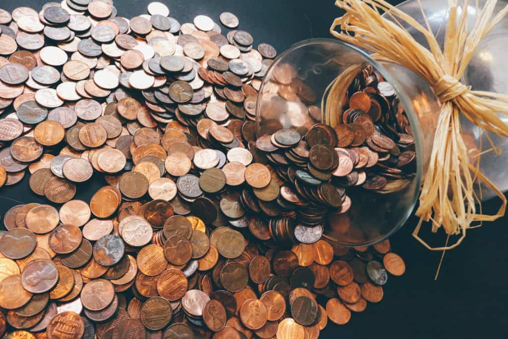 Glass jar spilling coins, representing value during economic challenges.