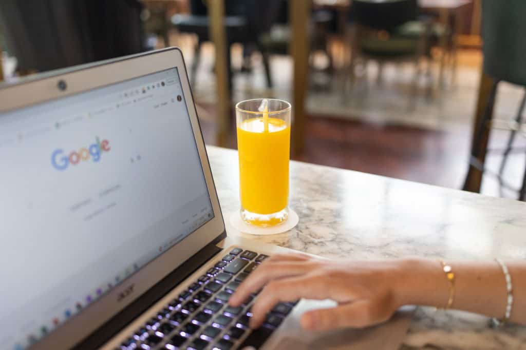 Person working on a laptop with Google search page open and a glass of orange juice.