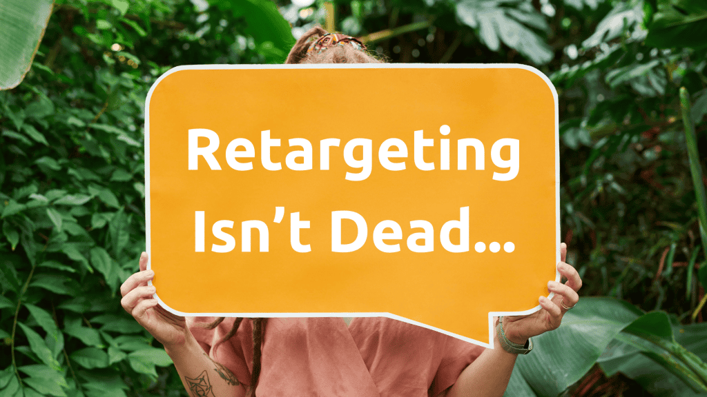 Person holding a speech bubble with "Retargeting Isn’t Dead" in a lush green environment.